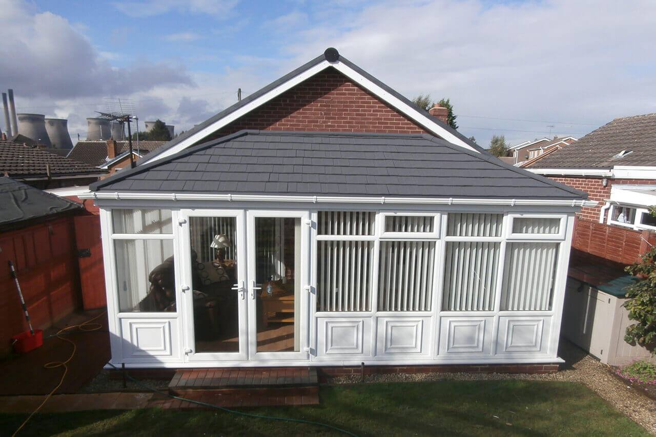 a white conservatory with a tiled roof on the back of a house