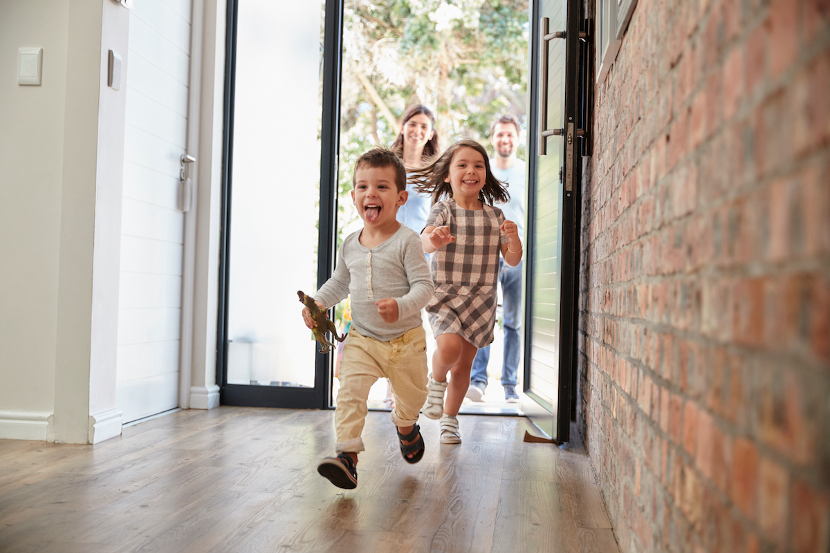 stock image of two children running through a front door with their parents following behind