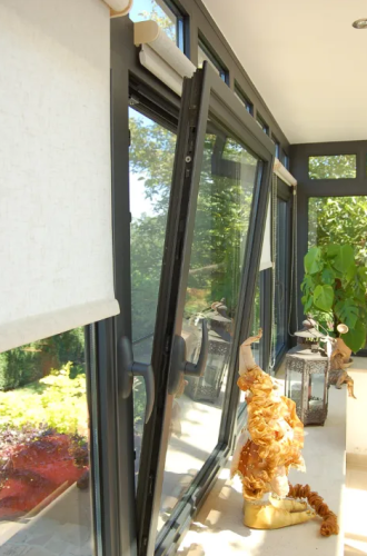 Black aluminium tilt and turn windows. They are open from the top for secure ventilation. There is a green garden beyond.