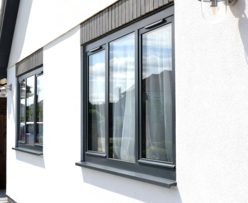 Black aluminium tilt and turn windows. They are closed. They are on a white house, and have three clear panes side by side. This image is taken from the outdoors.